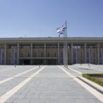 The Knesset parliament building in Jerusalem, Israel, with national flags at the main entrance.