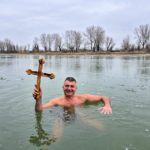 Man identified in the article as Ilija Srdanović holding a wooden cross while standing in icy water.