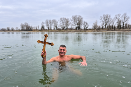Man identified in the article as Ilija Srdanović holding a wooden cross while standing in icy water.