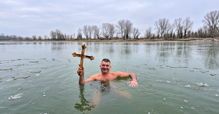 Man identified in the article as Ilija Srdanović holding a wooden cross while standing in icy water.
